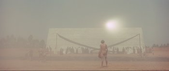 Movie still from “Fellini Satyricon” (1969), directed by Federico Fellini – A man standing on a beach in front of a crowd of onlookers; Extreme Wide shot, Low angle