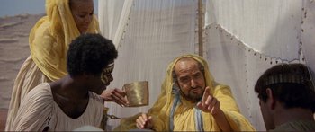 Movie still from “Fellini Satyricon” (1969), directed by Federico Fellini – A man in a yellow robe holding a cup and another man in a yellow robe holding a gold cup; Medium shot, Over the shoulder angle