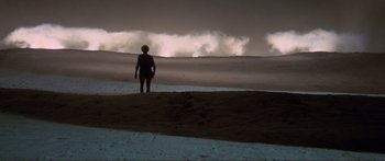 Movie still from “Fellini Satyricon” (1969), directed by Federico Fellini – A person standing on top of a hill near a body of water; Extreme Wide shot, High angle