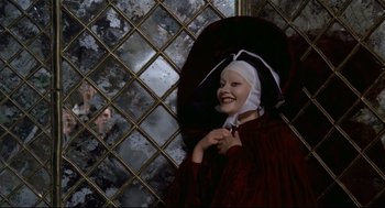 Movie still from “Fellini's Casanova” (1976), directed by Federico Fellini – A woman with a nun's head covering and a red umbrella in front of a mirrored wall; Medium shot, Over the shoulder angle
