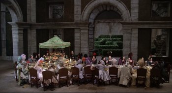 Movie still from “Fellini's Casanova” (1976), directed by Federico Fellini – A group of people sitting at a table with food on top of it; Extreme Wide shot, High angle
