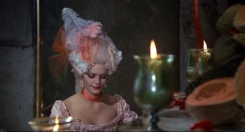 Movie still from “Fellini's Casanova” (1976), directed by Federico Fellini – A woman in a pink and white dress sitting at a dinner table; Medium shot, Over the shoulder angle