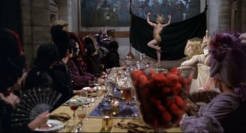 Movie still from “Fellini's Casanova” (1976), directed by Federico Fellini – A group of people sitting around a table with food on it; Wide shot, Over the shoulder angle
