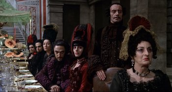 Movie still from “Fellini's Casanova” (1976), directed by Federico Fellini – A group of people sitting in a row wearing costumes; Medium shot, Over the shoulder angle