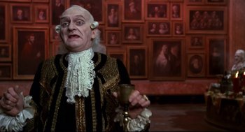 Movie still from “Fellini's Casanova” (1976), directed by Federico Fellini – An old man dressed in a costume holding a goblet in front of a wall of pictures; Medium shot, Low angle
