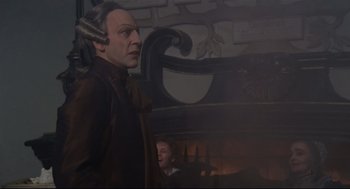 Movie still from “Fellini's Casanova” (1976), directed by Federico Fellini – A man in a brown jacket standing in front of a fireplace; Medium shot, Over the shoulder angle
