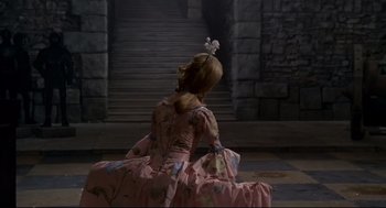 Movie still from “Fellini's Casanova” (1976), directed by Federico Fellini – A woman in a pink dress sitting in front of a stone wall; Wide shot, High angle