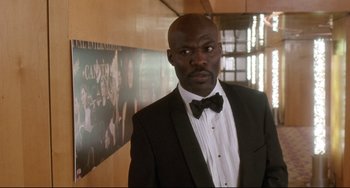 Movie still from “Femme Fatale” (2002), directed by Brian De Palma – A man in a tuxedo standing in front of a wall; Medium shot, Low angle