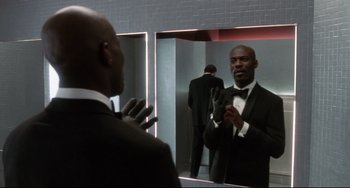 Movie still from “Femme Fatale” (2002), directed by Brian De Palma – A man in a suit looking at himself in the mirror; Medium shot, Low angle