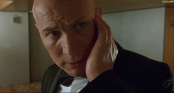 Movie still from “Femme Fatale” (2002), directed by Brian De Palma – A bald man in a suit and bow tie touching his ear; Close Up shot, Low angle