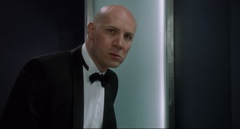 Movie still from “Femme Fatale” (2002), directed by Brian De Palma – A bald man in a black suit and a white shirt; Close Up shot, Low angle