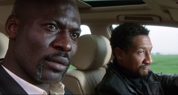Movie still from “Femme Fatale” (2002), directed by Brian De Palma – Two men sitting in the back seat of a car; Close Up shot, Low angle