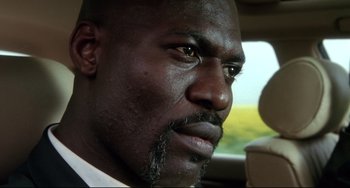 Movie still from “Femme Fatale” (2002), directed by Brian De Palma – A person in a car wearing a suit; Close Up shot, Low angle