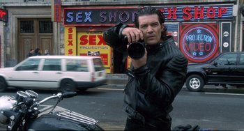 Movie still from “Femme Fatale” (2002), directed by Brian De Palma – A man in a leather jacket taking a picture on a motorcycle; Medium shot, Low angle