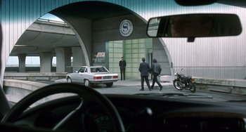 Movie still from “Femme Fatale” (2002), directed by Brian De Palma – A car parked on the side of the road with two men walking by; Wide shot, Over the shoulder angle