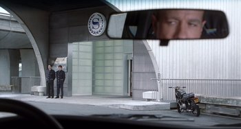 Movie still from “Femme Fatale” (2002), directed by Brian De Palma – A police officer is standing in front of a building; Wide shot, Over the shoulder angle