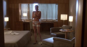 Movie still from “Femme Fatale” (2002), directed by Brian De Palma – A woman standing in a room with her arms crossed; Wide shot, Low angle