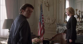 Movie still from “Femme Fatale” (2002), directed by Brian De Palma – A man standing in front of an american flag; Medium shot, Over the shoulder angle