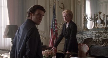 Movie still from “Femme Fatale” (2002), directed by Brian De Palma – A man and a woman standing in front of an american flag; Medium shot, Low angle