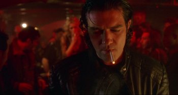 Movie still from “Femme Fatale” (2002), directed by Brian De Palma – A man smoking a cigarette in front of a group of people; Close Up shot, Low angle