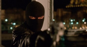 Movie still from “Femme Fatale” (2002), directed by Brian De Palma – A man in a black mask is standing in front of a building; Close Up shot, Low angle