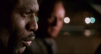 Movie still from “Femme Fatale” (2002), directed by Brian De Palma – A man looking at the camera while another man looks on; Close Up shot, Low angle