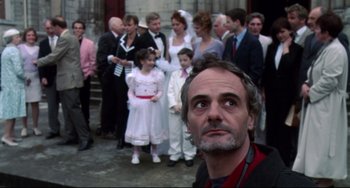 Movie still from “Femme Fatale” (2002), directed by Brian De Palma – A man standing in front of a group of people; Close Up shot, Low angle