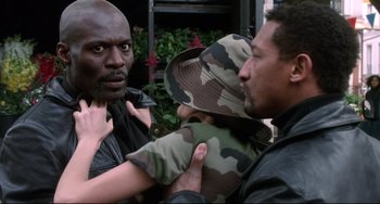 Movie still from “Femme Fatale” (2002), directed by Brian De Palma – A man holding a baby in his arms while another man looks on; Close Up shot, Over the shoulder angle