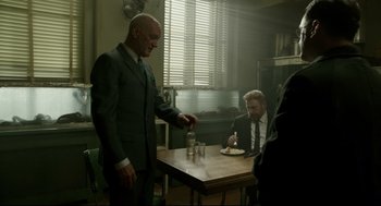 Movie still from “The Shape of Water” (2017), directed by Guillermo del Toro – A man in a suit and tie standing at a dinner table; Medium shot, Over the shoulder angle