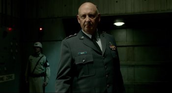 Movie still from “The Shape of Water” (2017), directed by Guillermo del Toro – An older man in a military uniform standing in front of a wall; Medium shot, Low angle