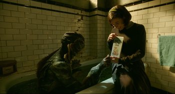 Movie still from “The Shape of Water” (2017), directed by Guillermo del Toro – A woman holding a book next to a dinosaur; Medium shot, High angle