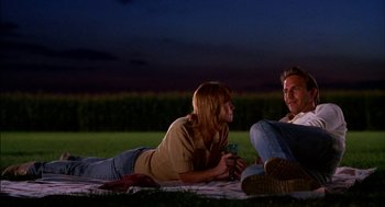 Movie still from “Field of Dreams” (1989), directed by Phil Alden Robinson – A man and a woman sitting on a blanket in the grass; Medium shot, Low angle