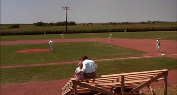 Movie still from “Field of Dreams” (1989), directed by Phil Alden Robinson – A man and a woman sitting on a bench watching a baseball game; Extreme Wide shot, High angle