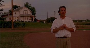 Movie still from “Field of Dreams” (1989), directed by Phil Alden Robinson – A man standing in front of a house on a dirt road; Medium shot, Low angle
