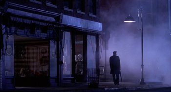 Movie still from “Field of Dreams” (1989), directed by Phil Alden Robinson – A man walking down the street holding an umbrella in front of a building; Wide shot, High angle