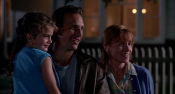 Movie still from “Field of Dreams” (1989), directed by Phil Alden Robinson – A man and a woman and a little girl smiling for the camera; Medium shot, Low angle