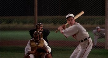 Movie still from “Field of Dreams” (1989), directed by Phil Alden Robinson – A man swinging a baseball bat on a baseball field; Medium shot, Over the shoulder angle