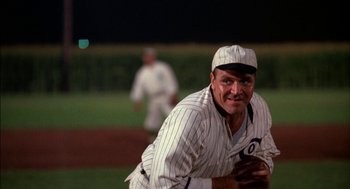 Movie still from “Field of Dreams” (1989), directed by Phil Alden Robinson – A man in a baseball uniform is smiling for the camera; Medium shot, Low angle