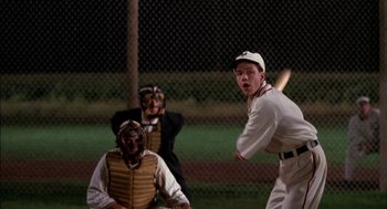 Movie still from “Field of Dreams” (1989), directed by Phil Alden Robinson – A man swinging a baseball bat at a game; Medium shot, Over the shoulder angle