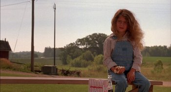 Movie still from “Field of Dreams” (1989), directed by Phil Alden Robinson – A young girl sitting on a bench eating a donut; Medium shot, Low angle