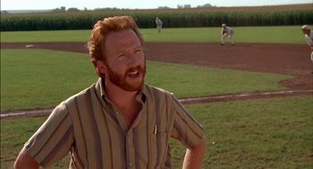 Movie still from “Field of Dreams” (1989), directed by Phil Alden Robinson – A man with red hair and a goatee standing on a baseball field; Close Up shot, Over the shoulder angle