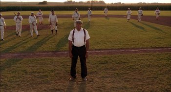 Movie still from “Field of Dreams” (1989), directed by Phil Alden Robinson – An older man in a baseball uniform stands in front of a group of men; Wide shot, Low angle