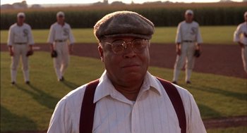 Movie still from “Field of Dreams” (1989), directed by Phil Alden Robinson – An older man wearing glasses and a hat; Medium shot, Low angle