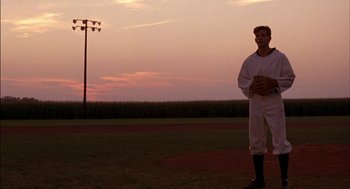 Movie still from “Field of Dreams” (1989), directed by Phil Alden Robinson – A baseball player standing on a baseball field at sunset; Wide shot, Over the shoulder angle