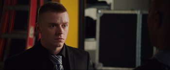 Movie still from “Fighting with My Family” (2019), directed by Stephen Merchant – A man wearing a suit and tie in front of a yellow wall; Close Up shot, High angle