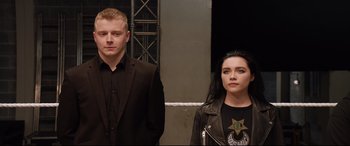 Movie still from “Fighting with My Family” (2019), directed by Stephen Merchant – A man and a woman standing next to each other in front of a building; Medium shot, Low angle