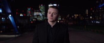 Movie still from “Fighting with My Family” (2019), directed by Stephen Merchant – A man in a black suit standing in front of a city skyline at night; Close Up shot, Low angle