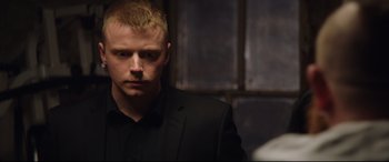 Movie still from “Fighting with My Family” (2019), directed by Stephen Merchant – A person wearing a suit and tie; Close Up shot, Over the shoulder angle