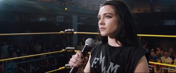 Movie still from “Fighting with My Family” (2019), directed by Stephen Merchant – A woman holding a microphone in front of a boxing ring; Close Up shot, Over the shoulder angle