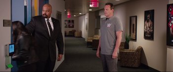 Movie still from “Fighting with My Family” (2019), directed by Stephen Merchant – Two men are standing in an office hallway; Medium shot, Over the shoulder angle